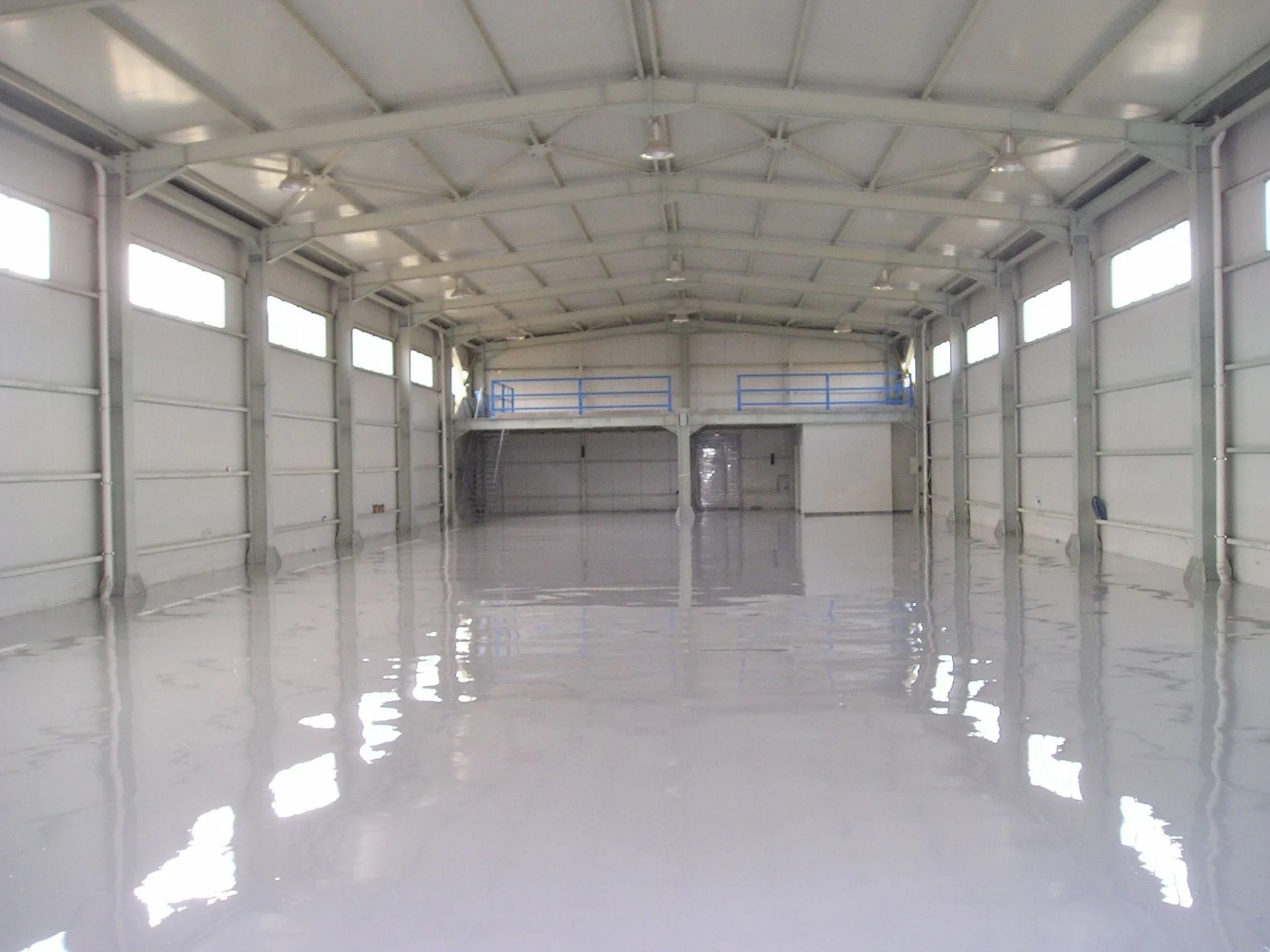 Glossy gray solid epoxy floor running the length of a steel warehouse, mezzanine catwalk above