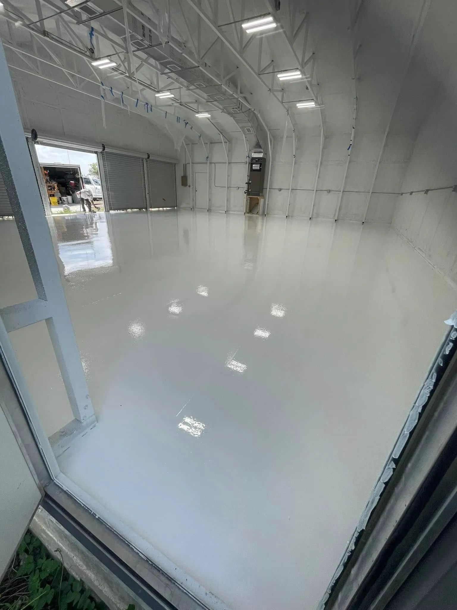 Glossy white solid epoxy floor in a large metal building with roll-up doors