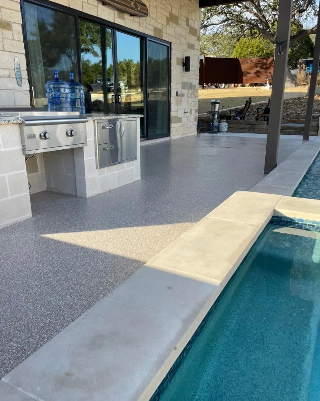 Textured gray pool-deck coating beside an outdoor kitchen