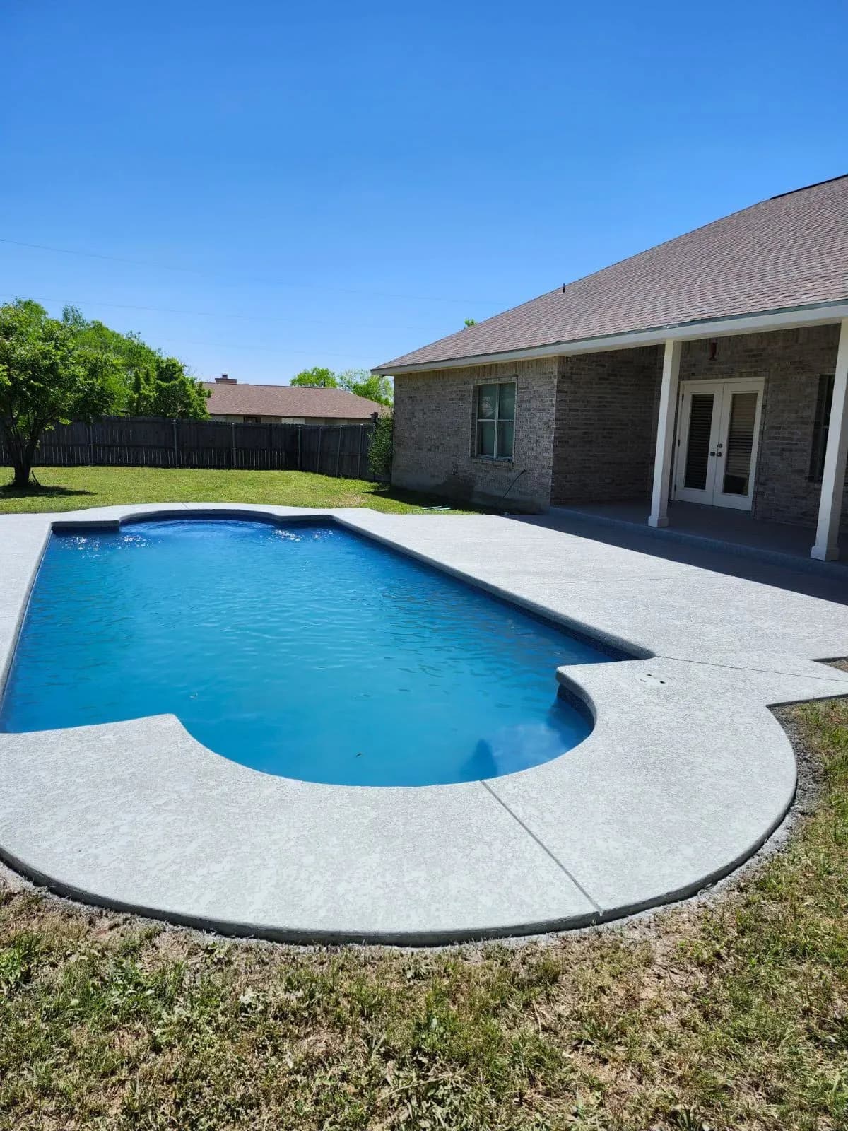 Light gray textured cool deck coating wrapping a backyard in-ground pool