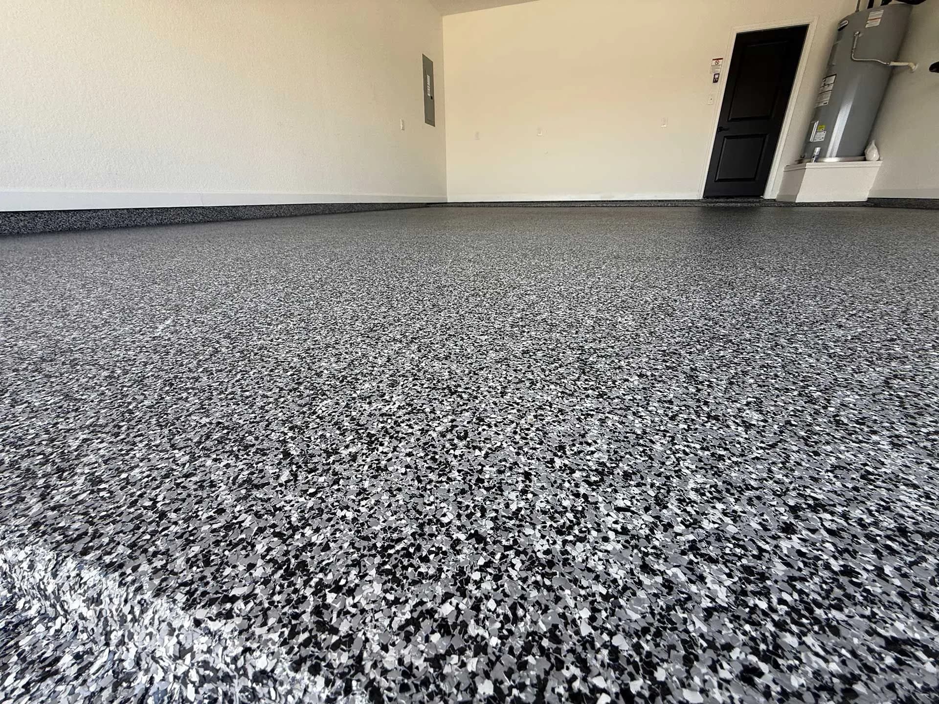 Charcoal, gray, and white flake epoxy garage floor, low angle across the slab toward a black door