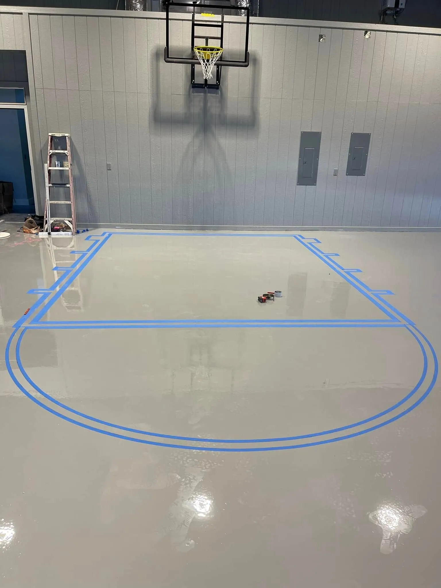 Gray solid epoxy court with blue tape marking the lines before the final coat