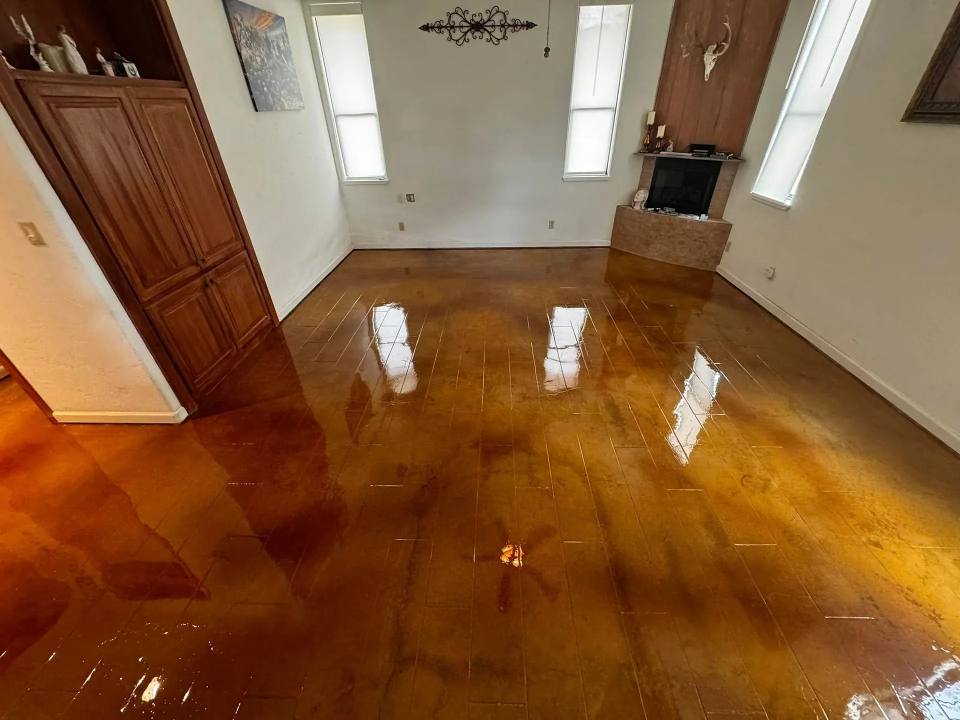 Glossy amber acid-stained concrete floor in a living room with a stone fireplace