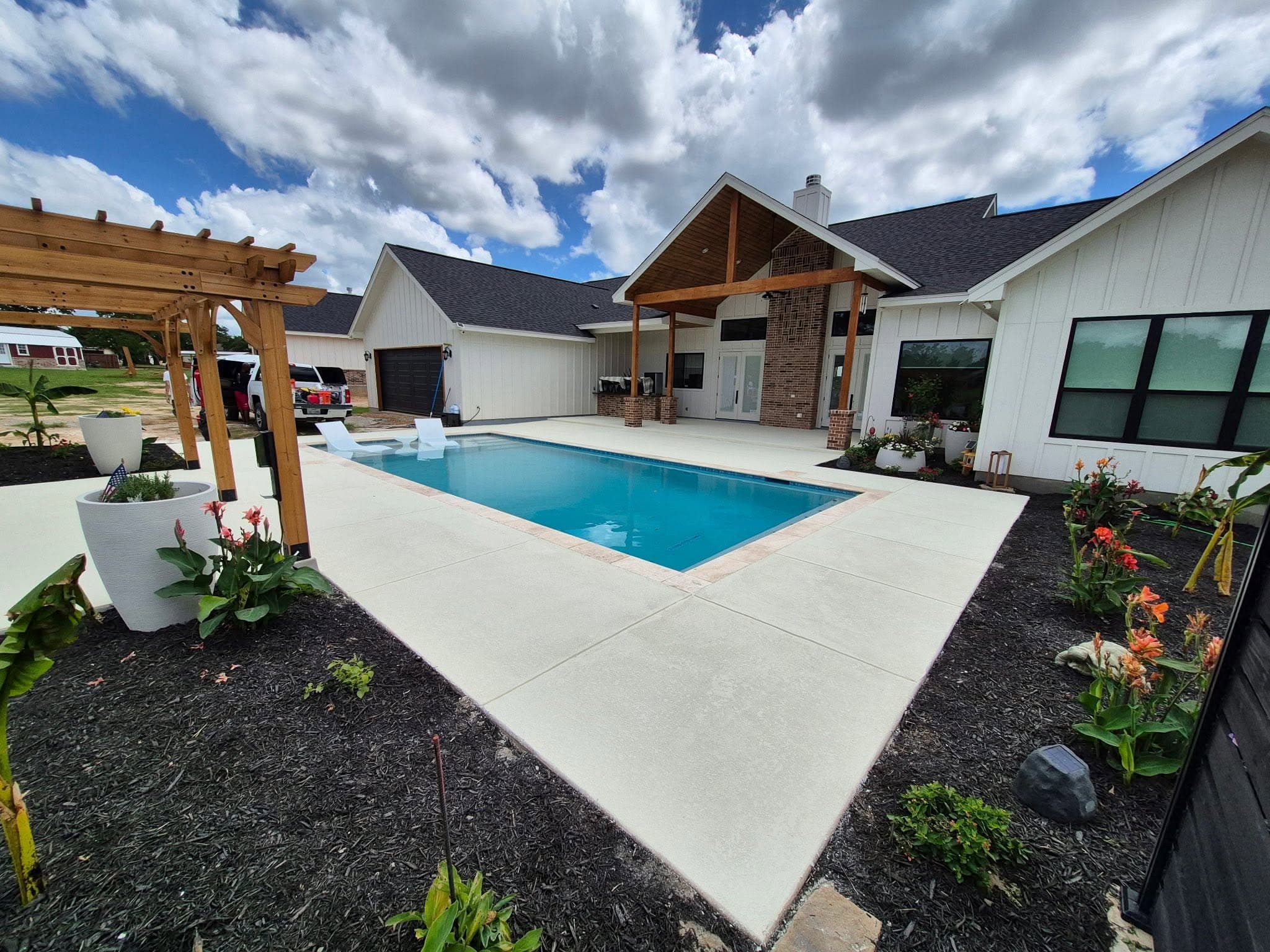 Tan cool deck finish wrapping a rectangular pool, pergola beyond
