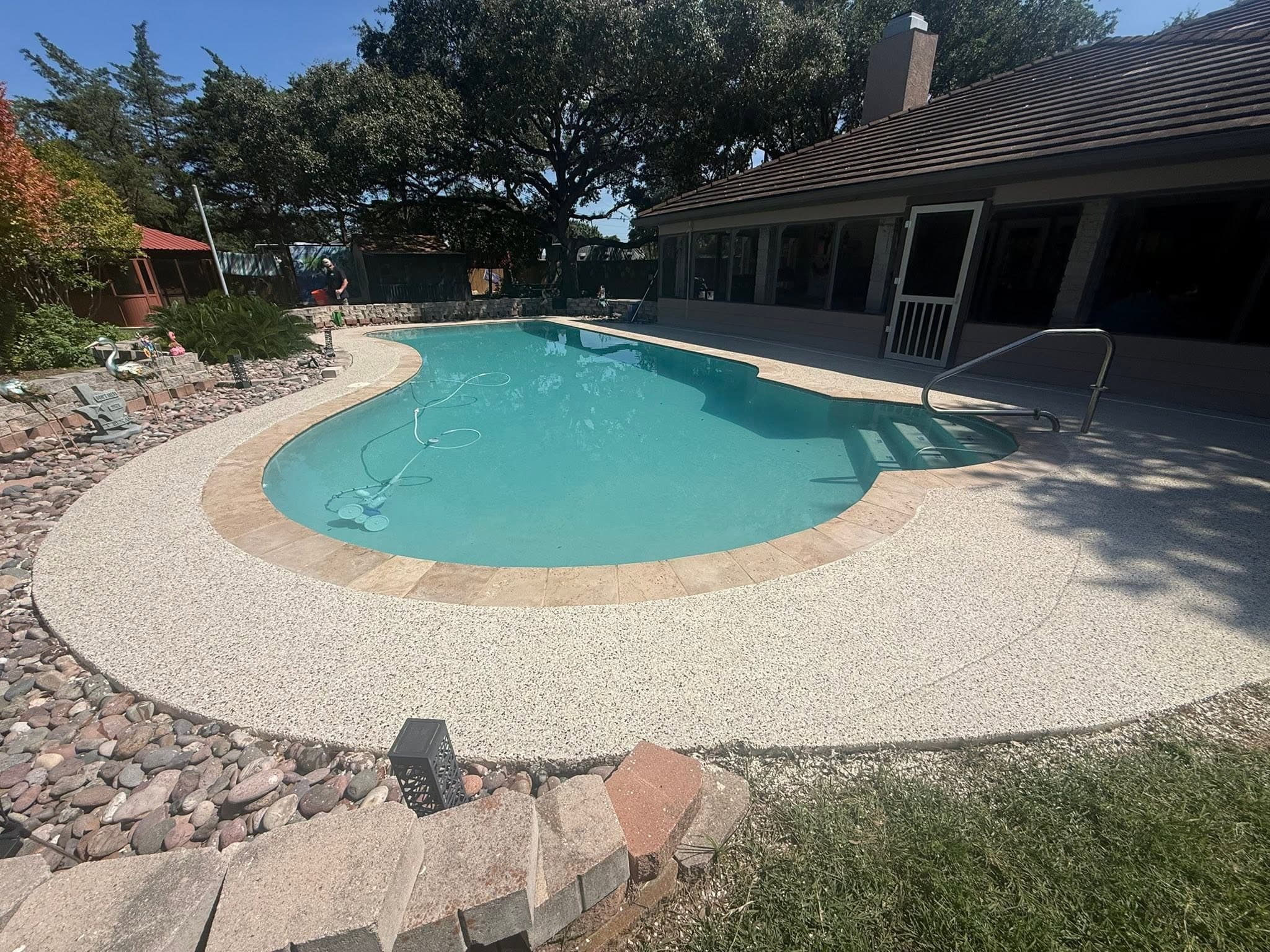 Resurfaced cream deck sweeping around a kidney pool with travertine coping