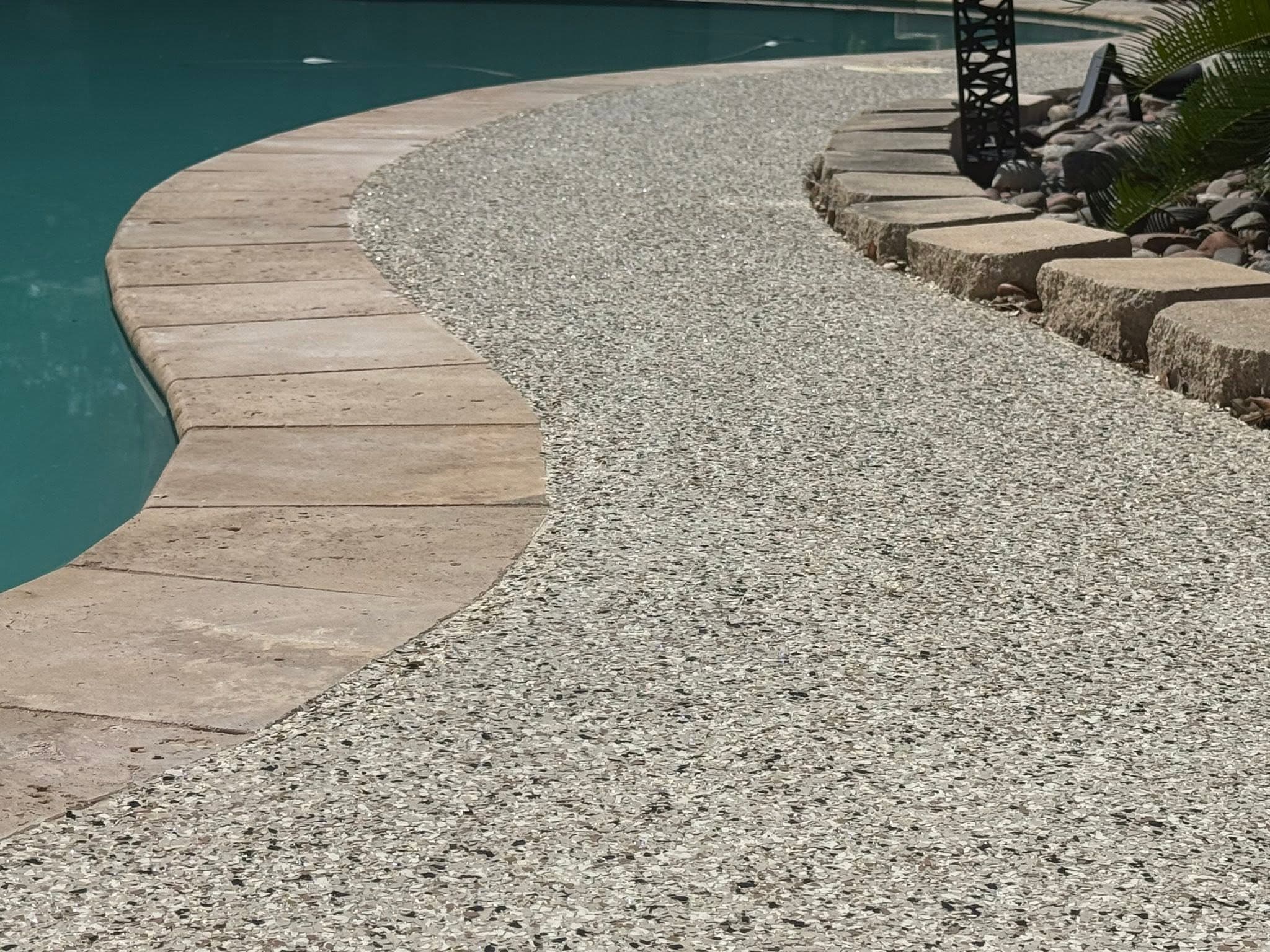 Speckled gray coated pool deck curving along travertine coping beside a turquoise pool